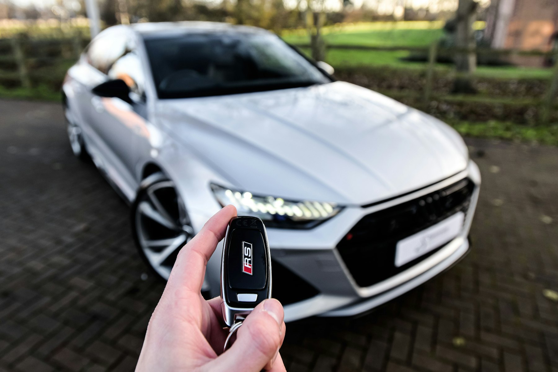 Hand hält einen Autoschlüssel vor einem silbernen Auto